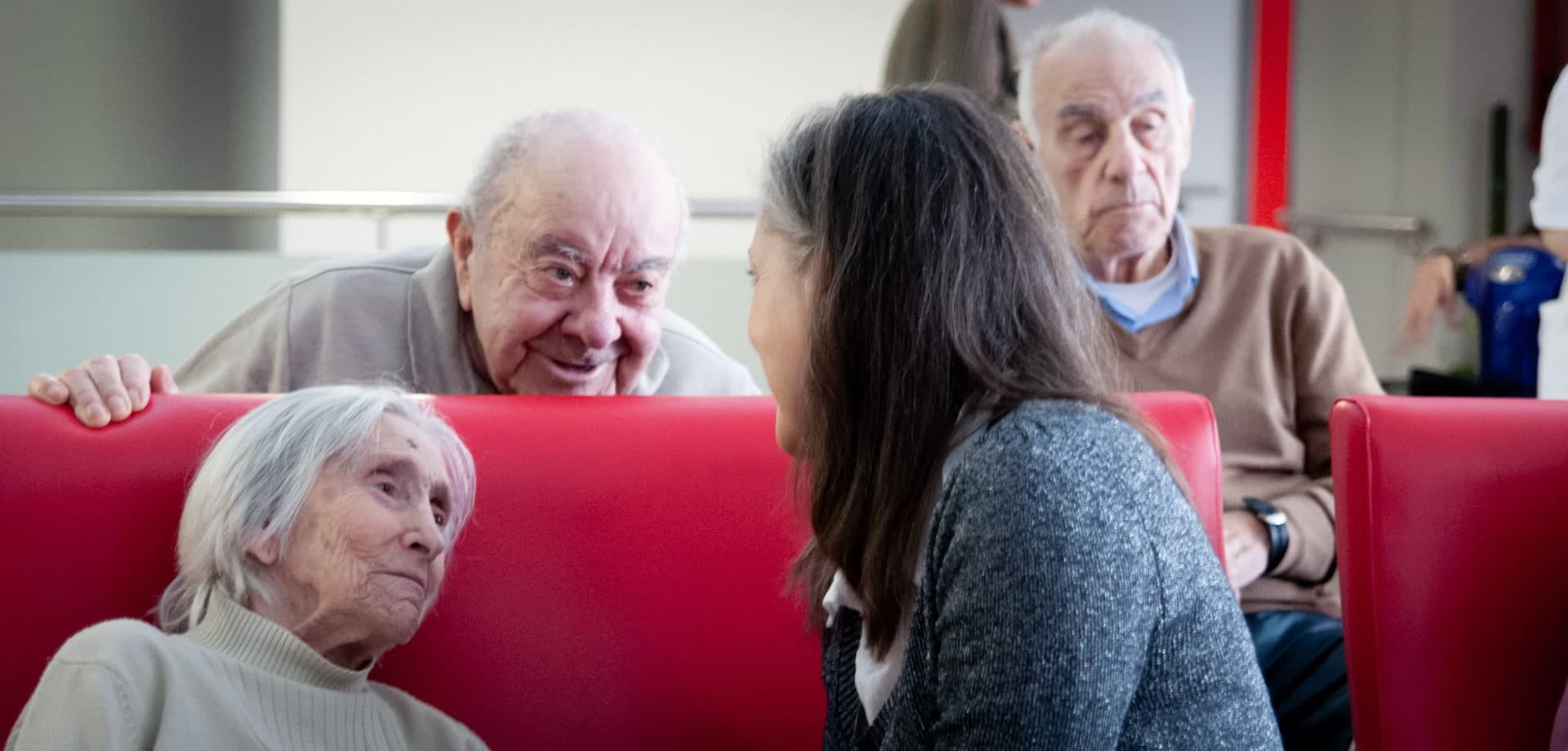 Varias personas mayores comparten un momento de conversación con una visitante en una residencia.